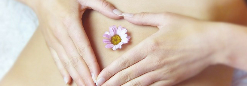 lady shaping her fingers into a love heart over her navel, which has a flower in it