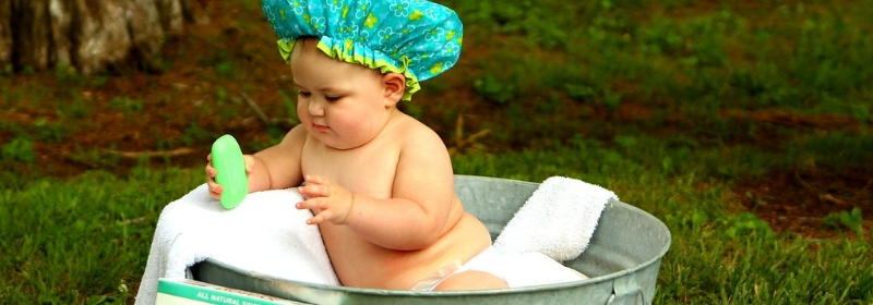 young baby having a bath with soap and wearing a shower cap